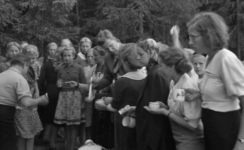 Naine kulbiga neiudele juua klaasi valamas looduses (Väljasõit mootorpaatidega, Tütarlastekool)