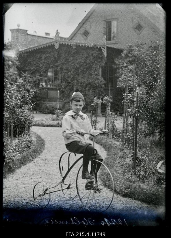Holzmeieri poeg kolmerattalisel jalgrattal aiateel, tagaplaanil elumaja.