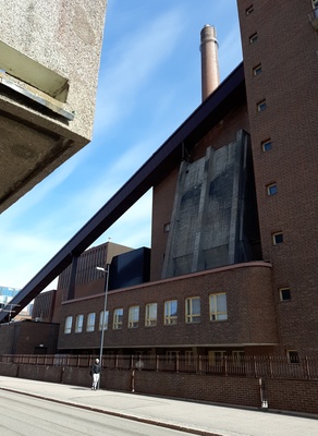 Osa Helsingin sähkölaitoksen Salmisaaren voimalaa, Lauttasaarenkatu 11 (nyk. Porkkalankatu 9-11), nähtynä Tallberginkadun varrelta, Porkkalankadun pohjoispuolelta. Voimalarakennuksen yläkertaan nousee hiiltä voimalan polttoaineeksi kuljettava linjasto. Voimala A otettiin käyttöön vuonna 1953. Valokuvan nurkissa näkyvät kaareutuvat tummat varjot, jotka johtuu siitä, että valokuvaaja on käyttänyt kuvatessaan vastavalosuojaa. rephoto