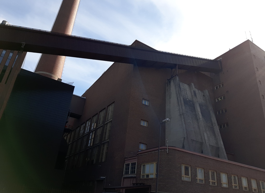 Osa Helsingin sähkölaitoksen Salmisaaren voimalaa, Lauttasaarenkatu 11 (nyk. Porkkalankatu 9-11), nähtynä Tallberginkadun varrelta, Porkkalankadun pohjoispuolelta. Rakennuksen yläkertaan nousee hiiltä voimalan polttoaineeksi kuljettava linjasto. Voimala A:n suunnitteli arkkitehti Vera Rosendal kaupunginarkkitehti Hilding Ekelundin johdolla, ja se otettiin käyttöön vuonna 1953. Valokuvan ylänurkissa näkyvät kaareutuvat tummat varjot, jotka johtuu siitä, että valokuvaaja on käyttänyt kuvatessaan vastavalosuojaa. rephoto