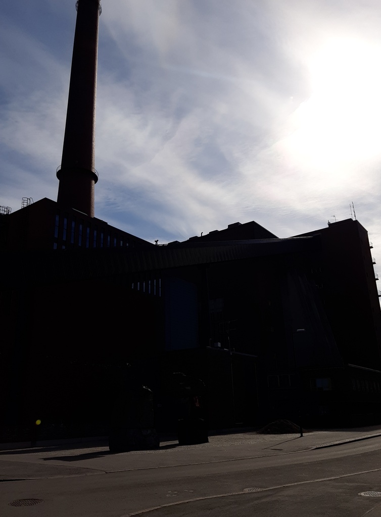 Helsingin sähkölaitoksen Salmisaaren voimala, Lauttasaarenkatu 11 (nyk. Porkkalankatu 9-11), nähtynä Tallberginkaun toiselta puolen, Porkkalankadun pohjoispuolelta. Rakennuksen savupiippu oli valmistuessaan ja pitkään sen jälkeenkin Helsingin korkein. Piipun editse rakennuksen yläkertaan nousee hiiltä polttoaineeksi kuljettava linjasto. Voimala A:n suunnitteli arkkitehti Vera Rosendal kaupunginarkkitehti Hilding Ekelundin johdolla, ja se otettiin käyttöön vuonna 1953. Valokuvan ylänurkissa näkyy kaareutuva tumma varjo, joka johtuu siitä, että valokuvaaja on käyttänyt kuvatessaan vastavalosuojaa. rephoto