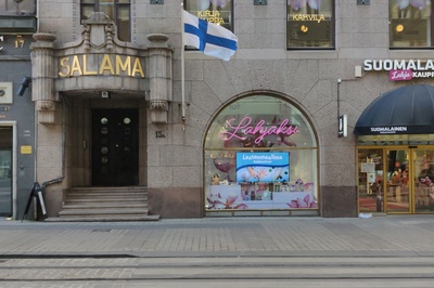 Salaman talo ja 1. kerroksen liikehuoneistoja. Kahdessa alimmassa kerroksessa on segmenttikaari-ikkunat. Julkisivun kummassakin reunassa on sisäänkäynti, ja näiden sivusisäänkäyntien yläpuolella lukee teksti Salama vakuutusyhtiö Salaman mukaan. Lisäksi näiden sisäänkäyntien yläpuolella on pienet parvekkeet. Liikehuoneiston vaatekaupan nimi Asu on kirjoitettu valokirjaimin jokaiseen kolmeen segmenttikaareen. Punainen pakettiauto on parkkeerattu vaatekaupan eteen sointuen vaatekaupan punaisiin valokiurjaimiin ja markiiseihin. Airam Electric Oy Ab:n  kuvamateriaalia. rephoto