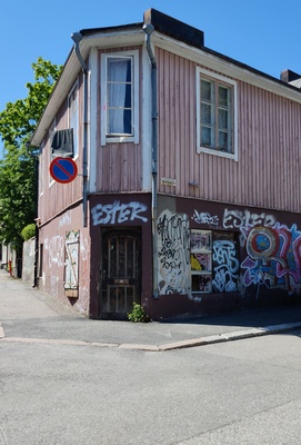 Lihaliike R. Laitinen Vallilantien ja Vanajantien kulmassa sijaitsevassa puutalossa Puu-Vallilassa. Liikkeen kyltissä ja ikkunaluukuissa on juomamainoksia. rephoto