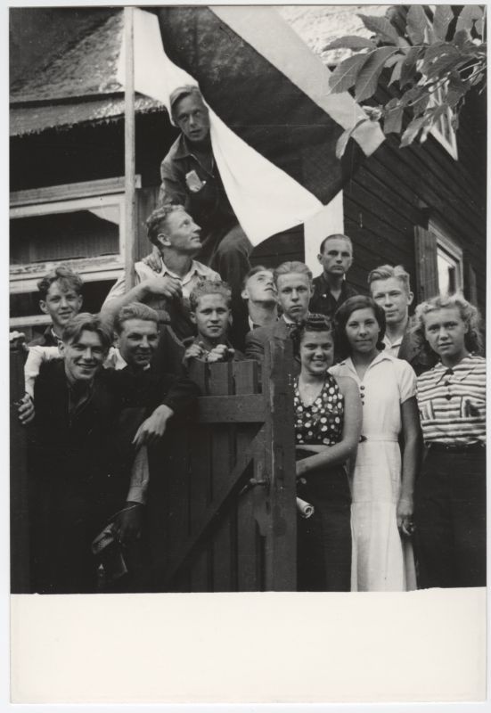 Noormehed ja tütarlapsed maja hoovis koos Eesti lipuga.