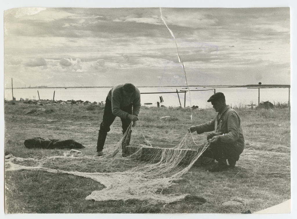 Kaks meest rannas lappamas suuresilmalist kalavõrku võrgukasti. Paremal paistmas Pandju saar.