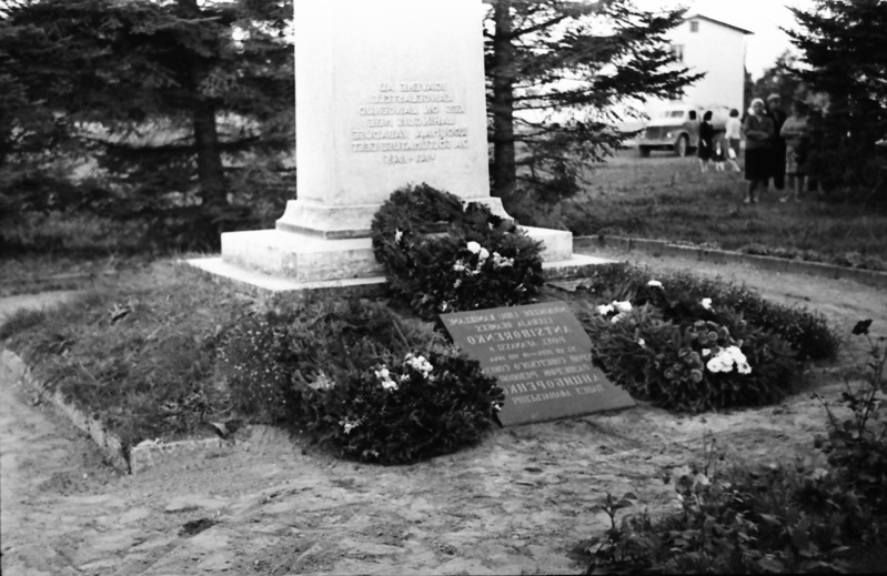 Monument ja tahvel esikülje vaates, jalamil pärjad.