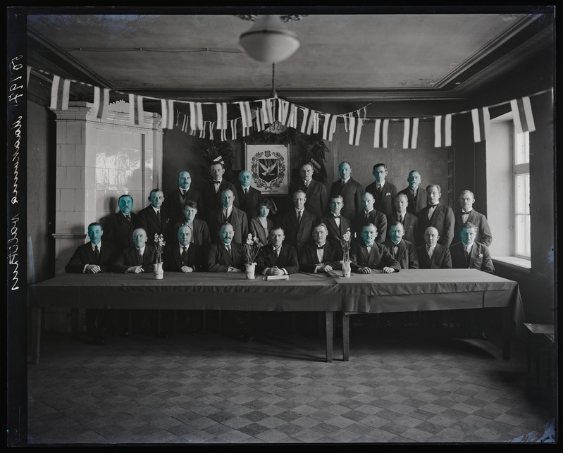 negatiiv Viljandi maavalitsus, grupp, osa laua taga sh maavanem H. Lauri, kaunistuseks lipud, seinal maakonna vapp, foto J. Riet, neg 50197, 24.02.1928