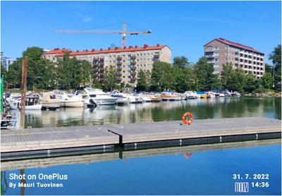 Taivallahden rantaa, Merikannontien ja Pohjoisen Hesperiankadun kulma. Etualalla laitureita ja veneitä, taustalla kerrostalot Merikannontie 3, 1 (Pohjoinen Hesperiankatu 37). rephoto