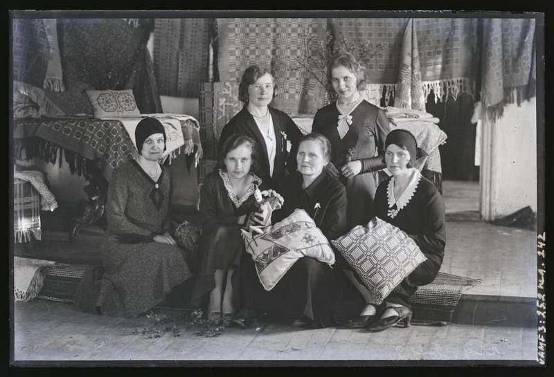 Grupp tundmatuid naisi (6 inimest) käsitöönäituse ees.