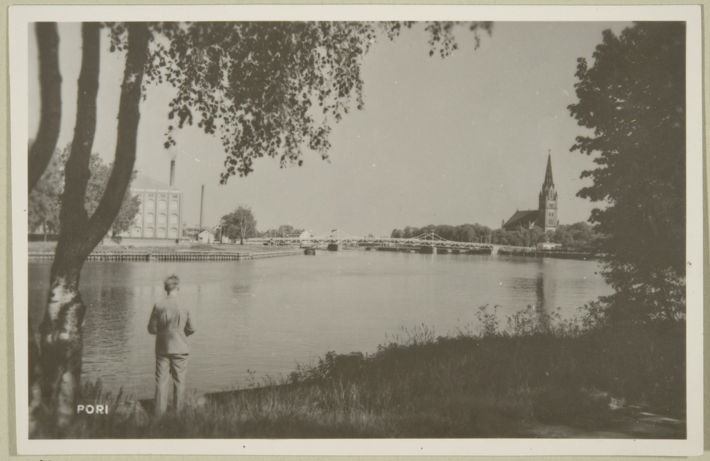 mies rannalla, taustalla vasemmalta Porin Puuvillan rakennuksia, silta ja Keski-Porin kirkko
