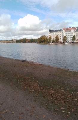 Kolme henkilöä nostamassa venettä Kaisaniemenlahden rannalla. Taustalla Pitkänsillanranta 13 - 17. rephoto