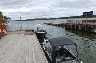 Retkeläiset menossa taksiveneeseen Vallisaaressa. Paikka on Torpedolahden laituri Vallisaaren itärannalla. Taivaanrannassa Haminansalmen toisella puolen näkyy Santahamina. rephoto