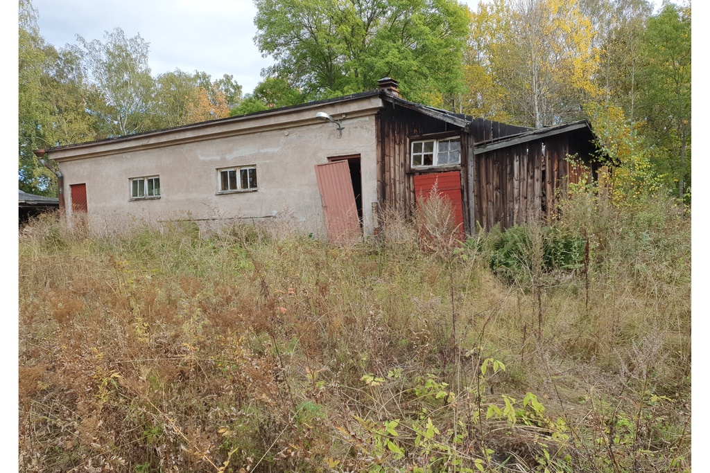 Paloaseman palokalustovaja Vallisaaressa. Siinä säilytettiin aikanaan T-mallista Fordia, kuorma-autoa ja hevosvetoisia kärryjä. Keskimmäisestä ovesta kuljettiin kahden hevosen talliin ja viereisestä punaisesta ovesta hevosten rehu- ja heinävarastoon. Pihapiiriin kuuluu myös vasemmassa reunassa näkyvä puusepänverstas. Valokuva on otettu aurinkoisella säällä. rephoto