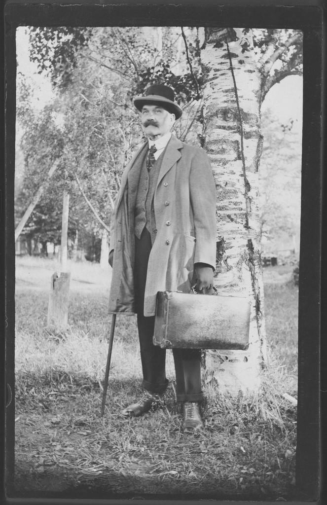 Negative of Akseli Gallen-Kallela, after coming home from Africa, with a suitcase and a walking stick in Tarvaspää garden, 1914.