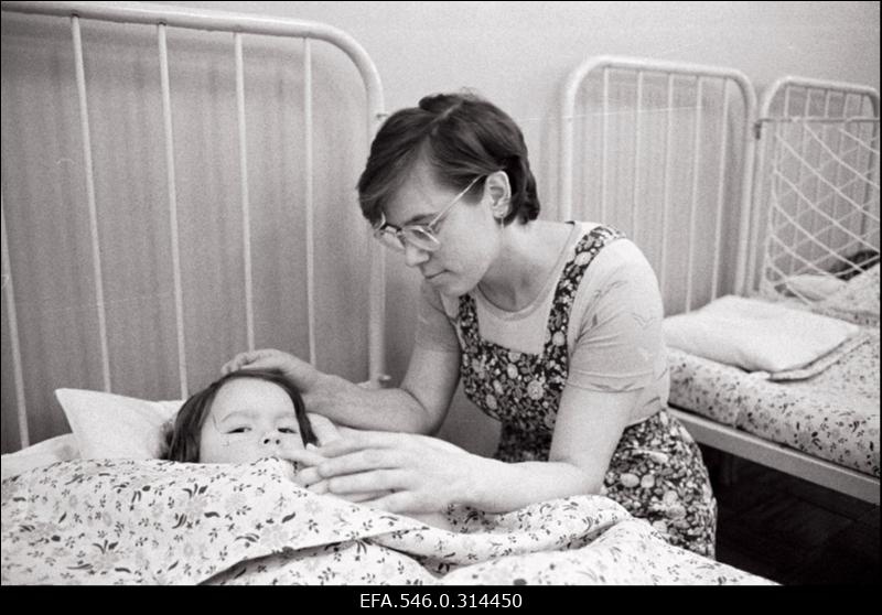 Laps voodis teki all. Hoolitsev käsi paitab lapse pead.