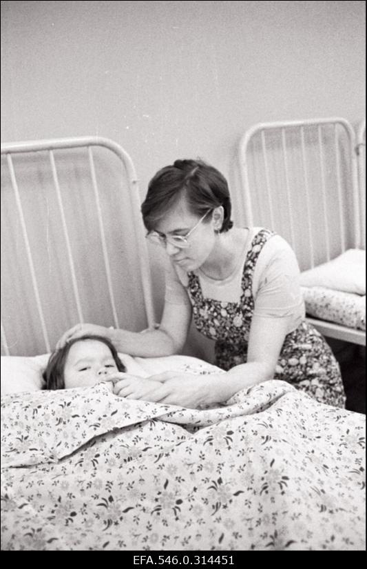 Laps voodis teki all. Hoolitsev käsi paitab lapse pead.