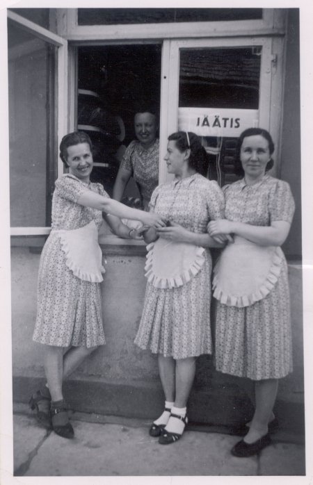 Foto. Kolm Dietrichi kohviku ettekandjat tänaval lahtise akna juures, kus müüakse jäätist.