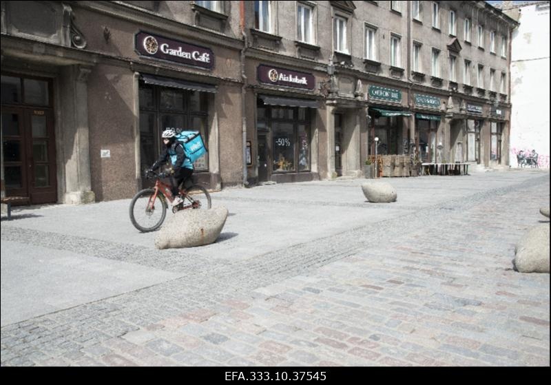 Vaade inimtühjale Kullassepa tänavale koroonapandeemia ajal.  Keskel jalgrattal Wolt toidukuller.