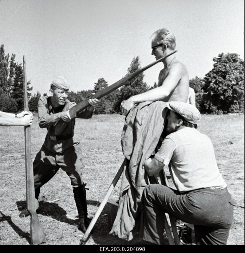 Tallinnfilmi mängufilmi "Inimesed sõdurisinelis" filmimine. Relva imitatsiooniga Kalju Komissarovit filmib operaator-lavastaja Mihhail Dorovatovski. Fookust veab operaatori assistent Mihkel Ratas.