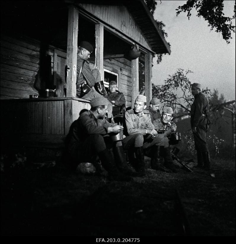 Stseen Tallinnfilmi mängufilmist "Inimesed sõdurisinelis". Istuvad all vasakult: Tääger (Heino Raudsik), Veski (ArviHallik), Raudnask (Hans Kaldoja), Enn Kalm (Rudolf Allabert). Terassil istuvad Agur (Tõnu Mikiver), Viies (Kenno Oja).