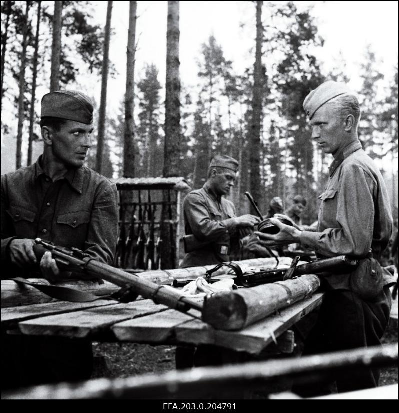 Stseen Tallinnfilmi mängufilmist "Inimesed sõdurisinelis". Sõjamehed tegelevad relvadega. Esiplaanil Kalm (Rudolf Allabert) ja Agur (Tõnu Mikiver).