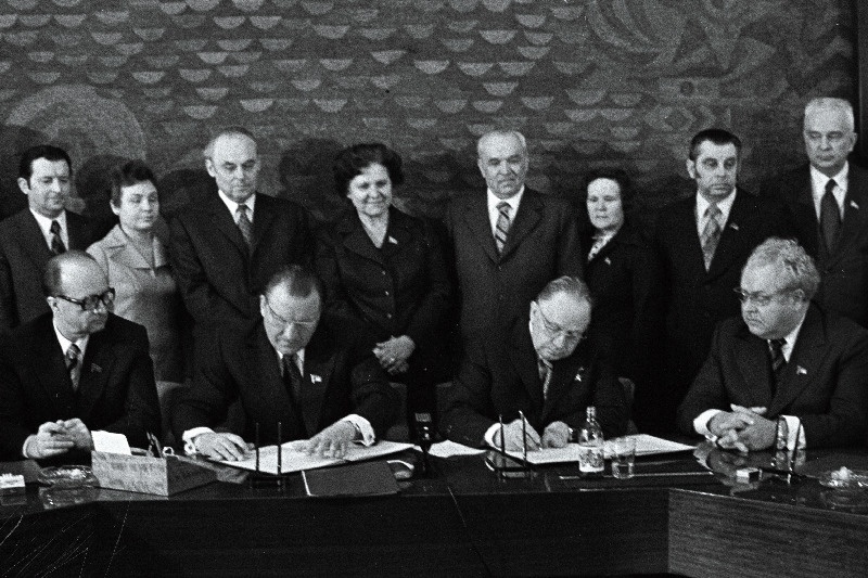 Eesti NSV ja Läti NSV töötajate 1976.a. sotsialistliku võistluse lepingule kirjutavad alla EKP Keskkomitee esimene sekretär J. Käbin (paremalt 2.) ja Läti KP Keskkomitee esimene sekretär A. Voss (paremalt 3.). Istub paremalt 1. NSV Ülemnõukogu Presiidiumi esimees A. Vader. Seisavad paremalt 1. ENSV Ministrite Nõukogu esimehe asetäitja V. Käo, 2. ENSV Ministrite Nõukogu esimehe esimene asetäitja E. Tõnurist, 5. ENSV Ülemnõukogu Presiidiumi esimehe asetäitja M. Vannas.