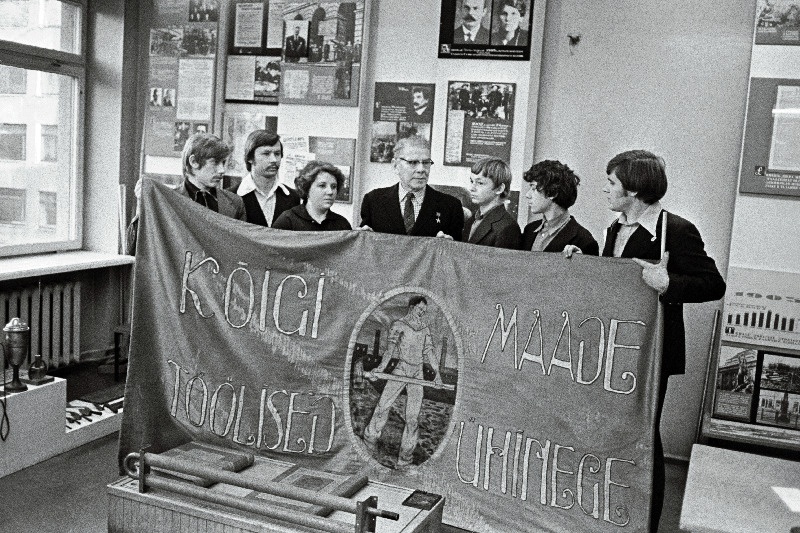 J. Lauristini nim. Tallinna Masinatehase tööveteran, sotsialistliku töö kangelane Alfred Valdov (keskel) näitab noortele töölistele 1917.a. võitluslippu.